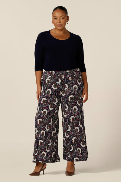 A 3/4 sleeve, round neck top in navy blue is worn with wide -leg, printed pants, shown on a size 18, plus size woman. Made in Australia by Australian and New Zealand women's clothing label, L&F, this slim fit top in stretch jersey fabric is a comfortable top for work wear or casual wear.