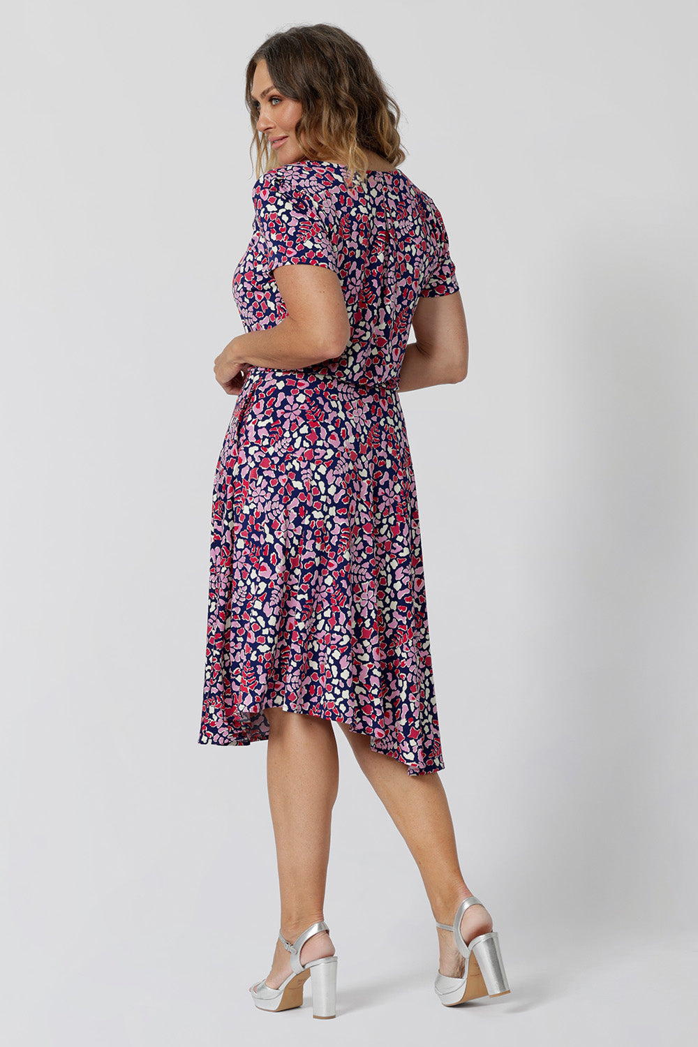 Back view of a summer dress for over 40s women. A size 12, over 40 woman wears knee length summer dress with asymmetric hemlineand cowl neck. A short sleeve dress in pretty red, pink, white and navy print this is a good jersey dress for travel and cruise wear. Made in Australia by Australian and New Zealand women's clothes brand, Leina & Fleur, shop their petite to plus size dresses online.