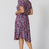 Back view of a summer dress for over 40s women. A size 12, over 40 woman wears knee length summer dress with asymmetric hemlineand cowl neck. A short sleeve dress in pretty red, pink, white and navy print this is a good jersey dress for travel and cruise wear. Made in Australia by Australian and New Zealand women's clothes brand, Leina & Fleur, shop their petite to plus size dresses online.