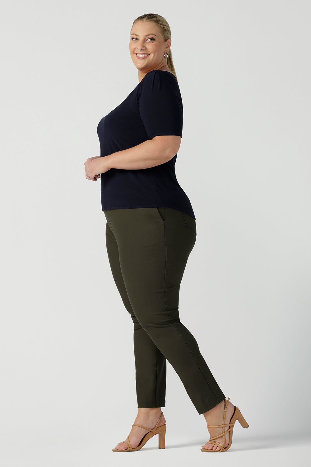 A good top for plus size, curvy women, this short sleeve, boat neck top in navy blue is worn with slim leg, olive green pants by a size 18 woman. A quality top for workwear, this slim fit jersey top is made in Australia by women's clothing brand, Leina & Fleur.