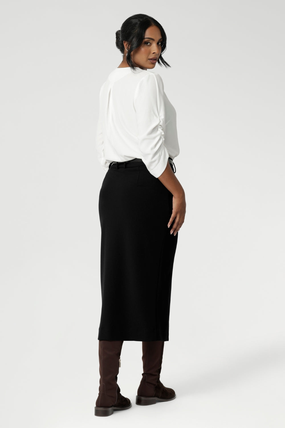 Back view image of Australian made black workwear skirt seen on over 30's woman paired with white blouse and brown boots for an elevated workwear look. Sizes 8-24 available at Leina & Fleur.