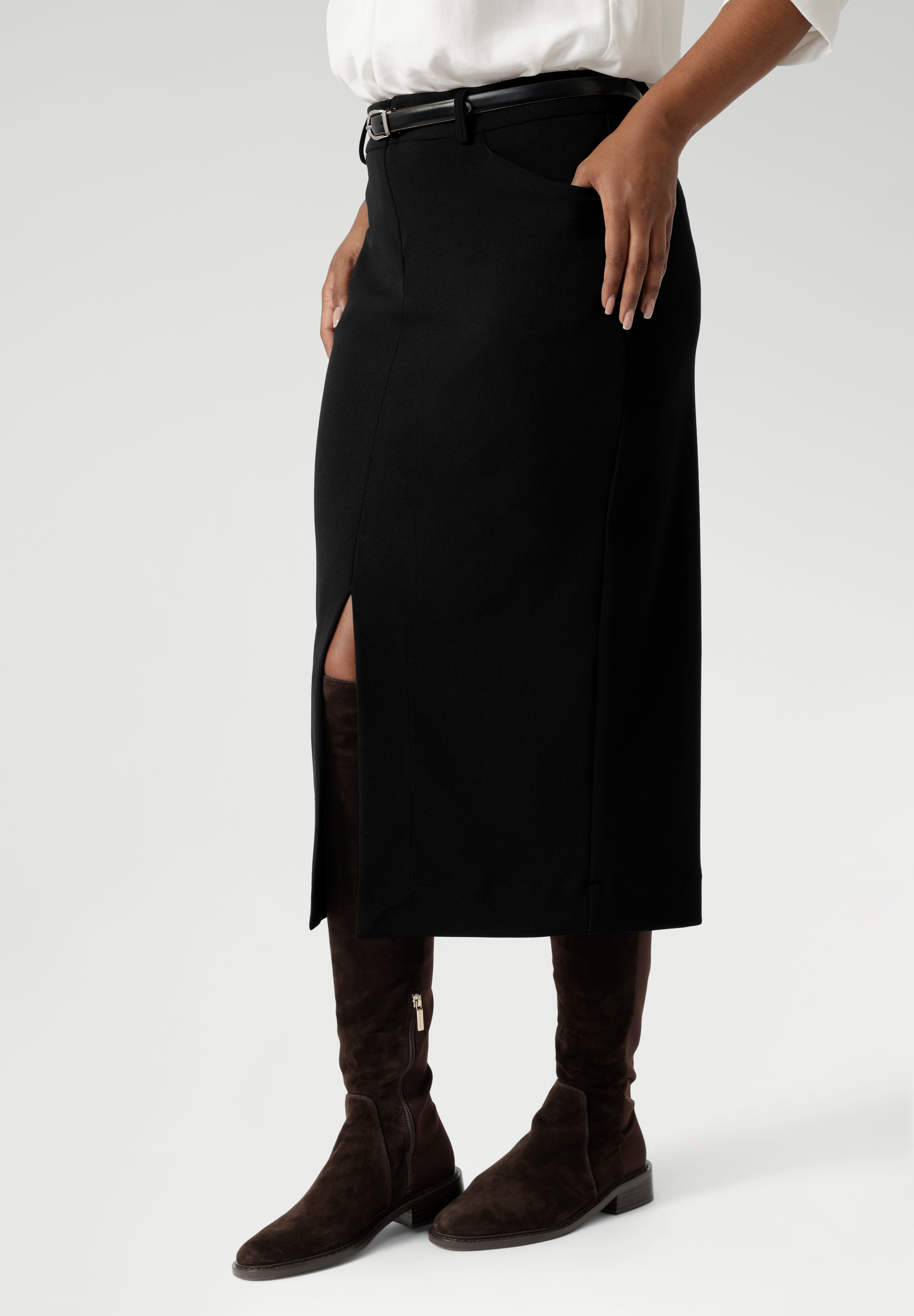 Close up image of Made in Australia by Australian and New Zealand women's clothing brand, Leina & Fleur. This stretchy, easy-care skirt is a perfect workwear piece for elevated suit styling with matching jacket or blazer. Size 10 model wears her midi length workwear skirt with long boots and a white collared blouse.