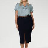 Full body front view of 40 year old plus sized woman wearing a midi length work skirt. This workwear skirt is navy in colour and made of good quality scuba crepe fabric. This skirt has an above the knee slit for comfort and mobility. Perfect skirt for an office or corporate setting. 3/4 length skirt is Australia made by New Zealand and Australian women. Leina & Fleur is a clothing company for woman that stock sizes from 8 to 24. Shop this work skirt in plus sizes and petite sizes.