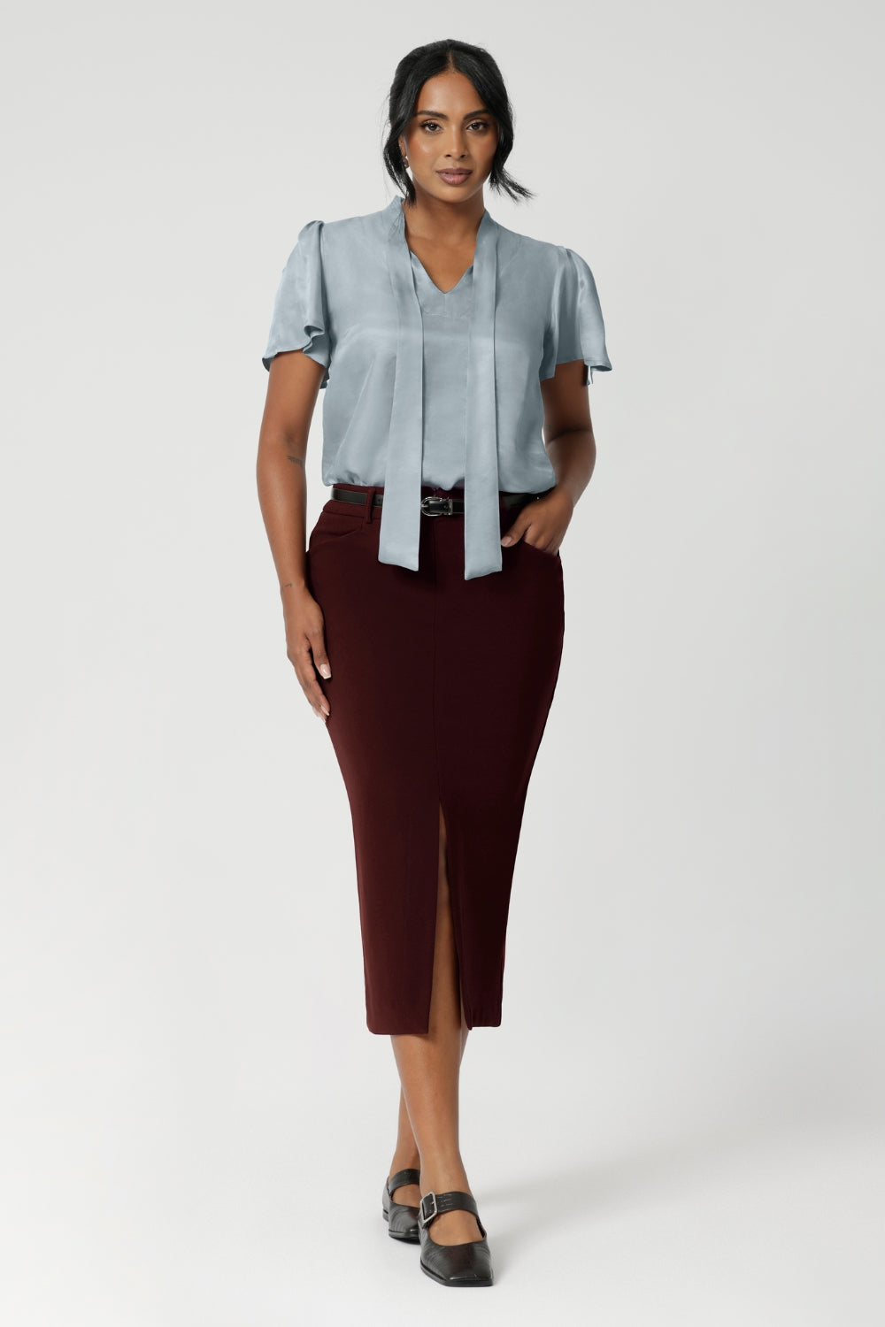 Designed with a mid-rise fit, the skirt features a waistband with belt loops for added versatility in styling. Size 10 woman wears her Aaron skirt with blouse tucked in and a matching brown belt and ballet flat.