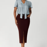 Designed with a mid-rise fit, the skirt features a waistband with belt loops for added versatility in styling. Size 10 woman wears her Aaron skirt with blouse tucked in and a matching brown belt and ballet flat.