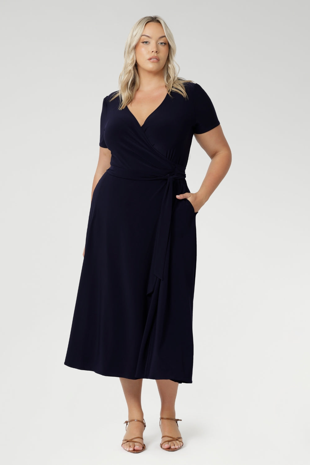 A curvy, size 18 woman wearing a navy, wrap dress with short sleeves. A great dress for summer casual wear, or for travel. Shop made in Australia dresses in petite to plus sizes online at Australian fashion brand, Leina & Fleur.