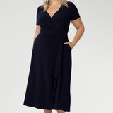 A curvy, size 18 woman wearing a navy, wrap dress with short sleeves. A great dress for summer casual wear, or for travel. Shop made in Australia dresses in petite to plus sizes online at Australian fashion brand, Leina & Fleur.