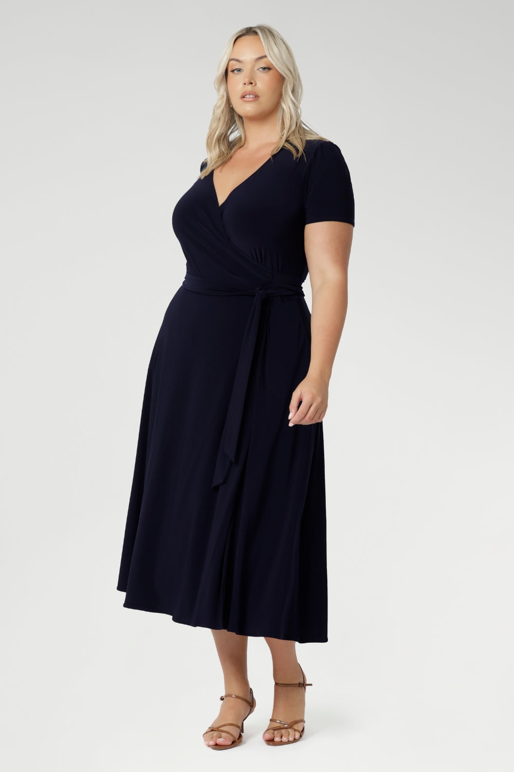 A curvy, size 18 woman wearing a navy, wrap dress with short sleeves. A great dress for summer casual wear, or for travel. Shop made in Australia dresses in petite to plus sizes online at Australian fashion brand, Leina & Fleur.