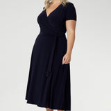 A curvy, size 18 woman wearing a navy, wrap dress with short sleeves. A great dress for summer casual wear, or for travel. Shop made in Australia dresses in petite to plus sizes online at Australian fashion brand, Leina & Fleur.