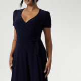A curvy, size 18 woman wearing a navy, wrap dress with short sleeves. A great dress for summer casual wear, or for travel. Shop made in Australia dresses in petite to plus sizes online at Australian fashion brand, Leina & Fleur.