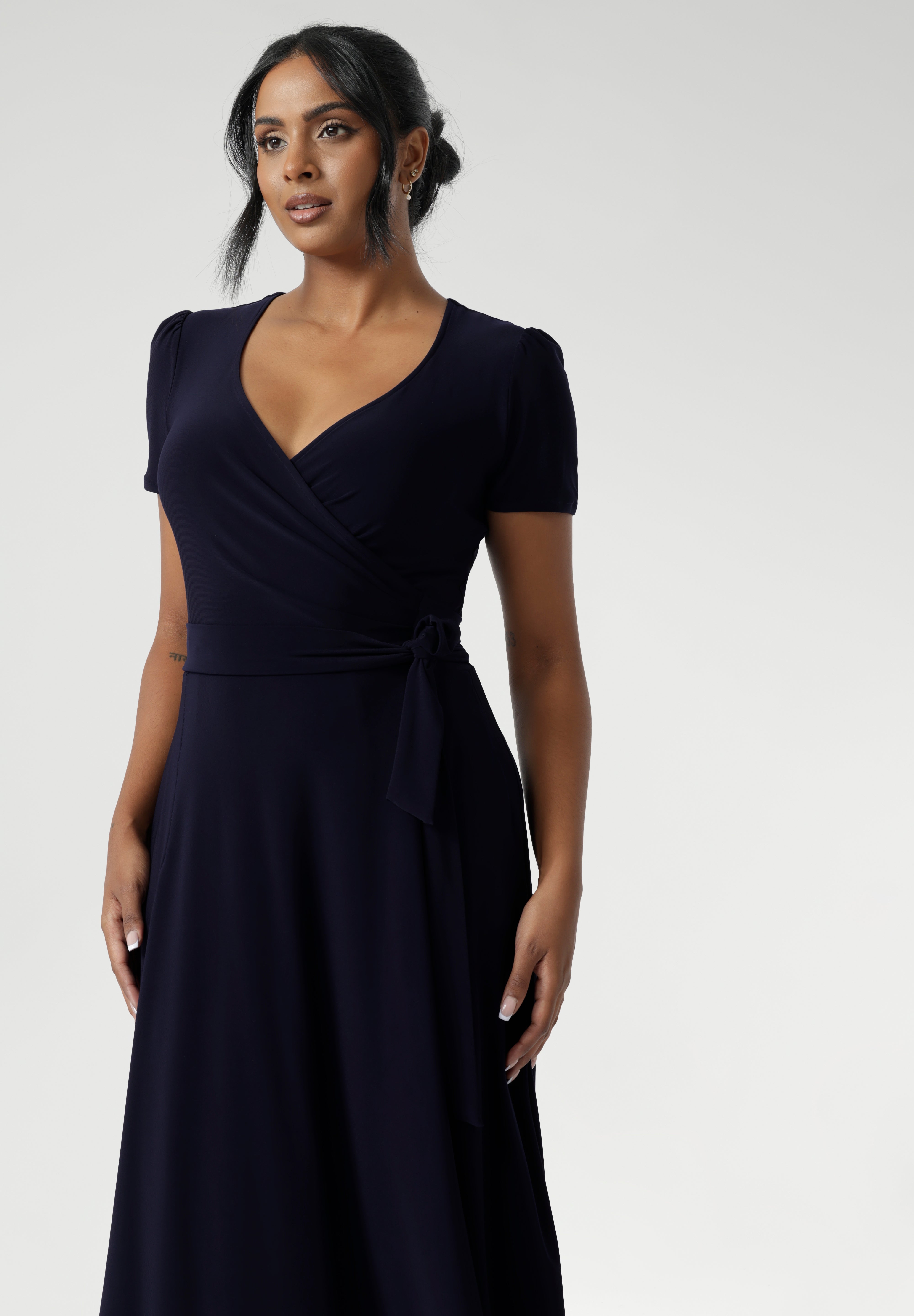 A curvy, size 18 woman wearing a navy, wrap dress with short sleeves. A great dress for summer casual wear, or for travel. Shop made in Australia dresses in petite to plus sizes online at Australian fashion brand, Leina & Fleur.