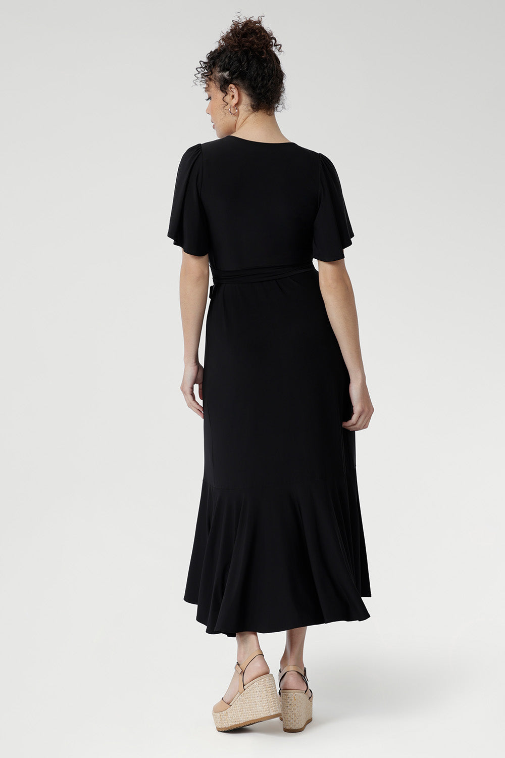 Black jersey wrap dress with extended waist ties, sweetheart neckline, and feminine flutter sleeves — perfect for events and celebrations.