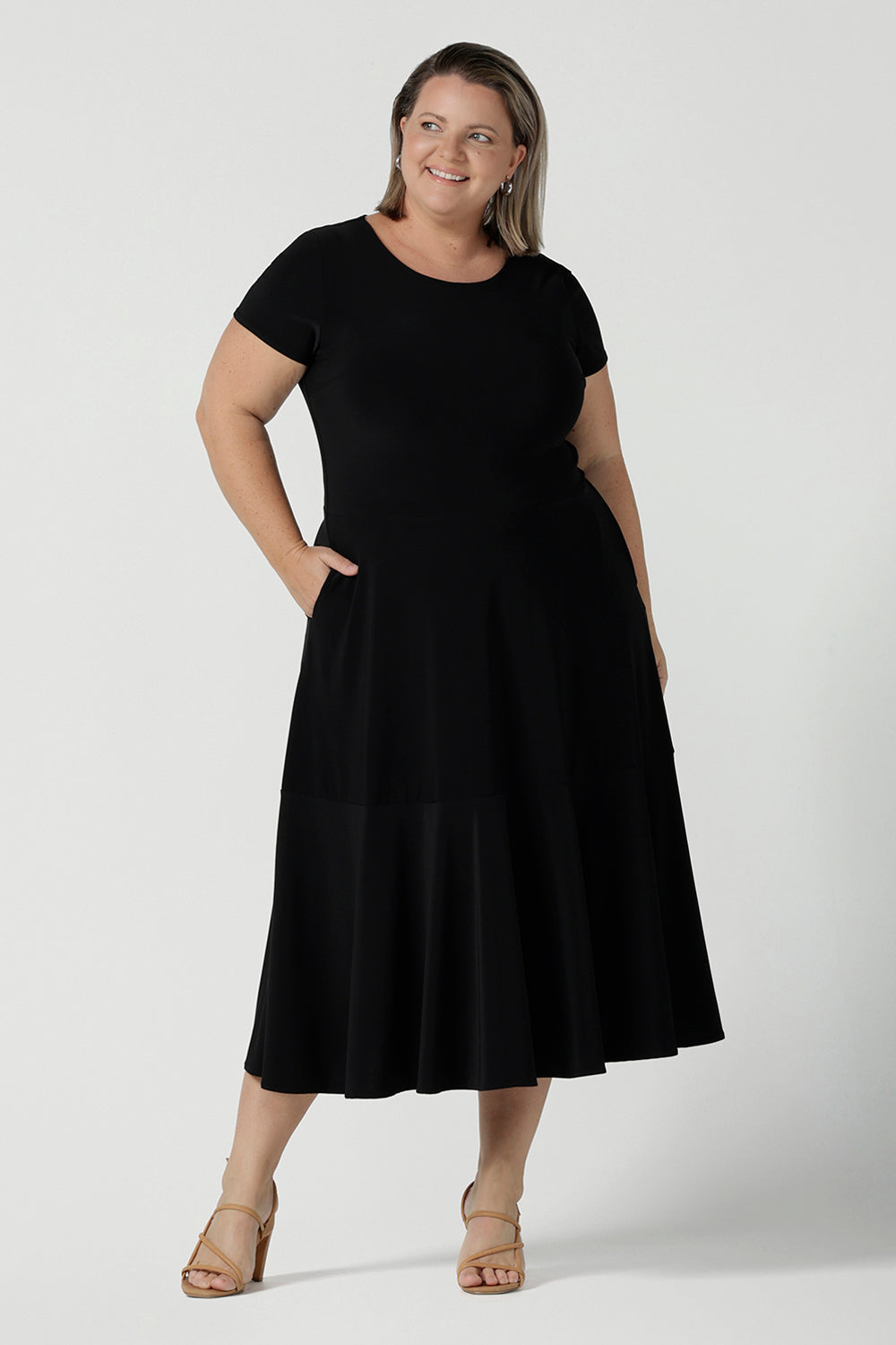 A size 18 woman wears the Amal dress in black is a slim fit round neck dress with waist seam and tier at the bottom. Functioning pockets. Great for work or event occasions. Made in Australia. Size inclusive fashion for women size 8 - 24.