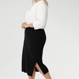Size 18 woman wears Andi Midi Skirt in Black is designed in a sophisticated mid-calf length with a flattering side-split, making it perfect for both work and events.