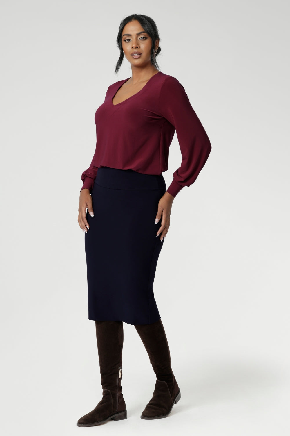 The Andi Tube Skirt in Navy is a key piece from our luxe mix-and-match separates collection, offering versatility for office, travel, or weekend styling. Size 10 model wears her navy midi tube skirt with ruby coloured top and long brown boats.