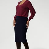 The Andi Tube Skirt in Navy is a key piece from our luxe mix-and-match separates collection, offering versatility for office, travel, or weekend styling. Size 10 model wears her navy midi tube skirt with ruby coloured top and long brown boats.