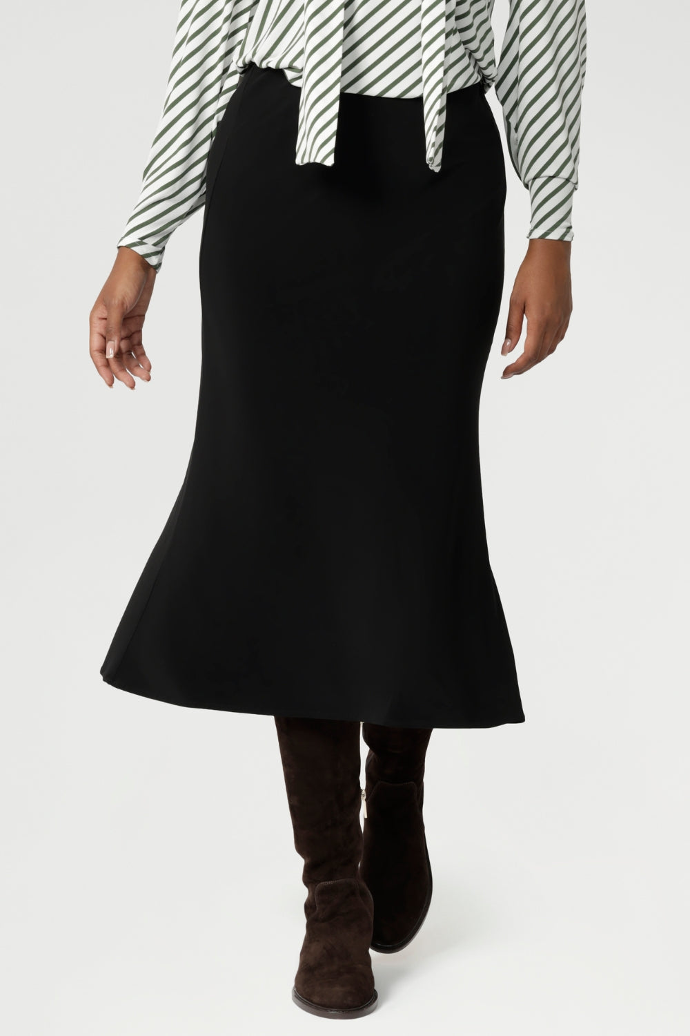 Women's black sleek midi skirt with streamlined design, can easily be dressed up for a more elevated look or worn casually - making it a truly versatile wardrobe staple for your everyday. Size 10 model pairs black midi skirt with olive striped white top and a long brown boots.