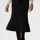 Women's black sleek midi skirt with streamlined design, can easily be dressed up for a more elevated look or worn casually - making it a truly versatile wardrobe staple for your everyday. Size 10 model pairs black midi skirt with olive striped white top and a long brown boots.
