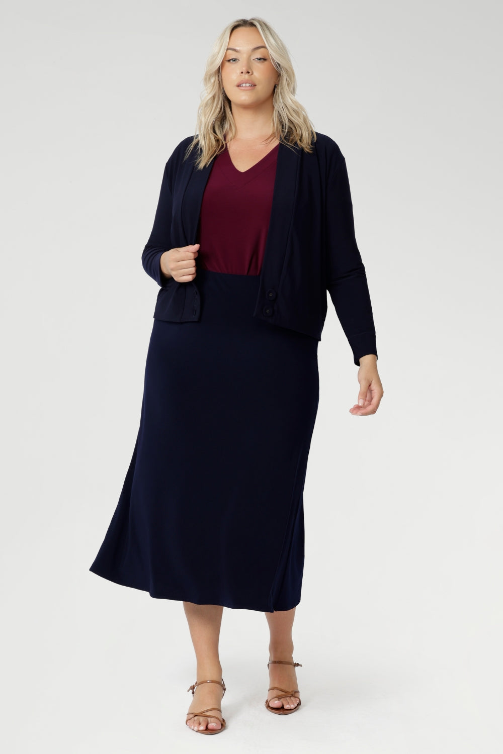 Australian-made midi skirt is crafted from a soft-touch jersey fabric, offering a lightweight feel that's perfect for all-day comfort. Plus size model wears travel ready skirt in deep navy colour paired with ruby coloured top and navy sandro.