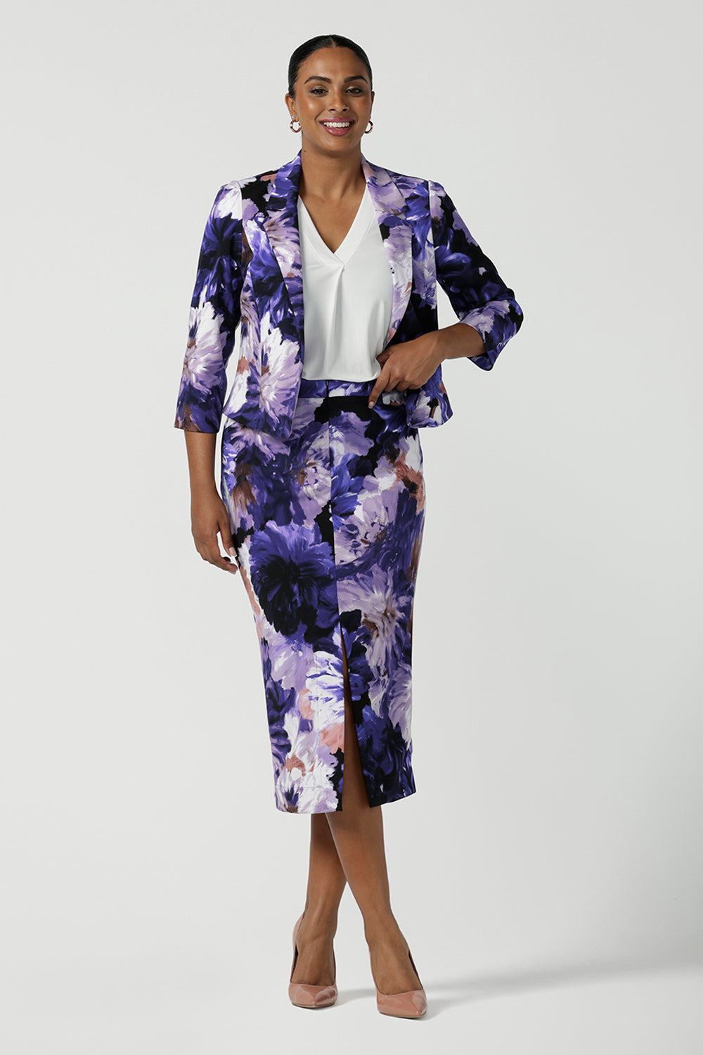 Back view of a size 10 woman wears the Aaron Midi Skirt in Jacaranda. A printed Midi length skirt in purple florals. Made in Australia for women size 8-24. Styled back with pink pumps and a purple Jacaranda jacket.