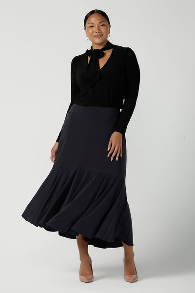 A size 12 woman wears the Thom top in Black a tie neck top with a V-neckline. Made in comfortable jersey have and made in Australia for women size 8 - 24. Styled back with a Berit Maxi Skirt in Charcoal