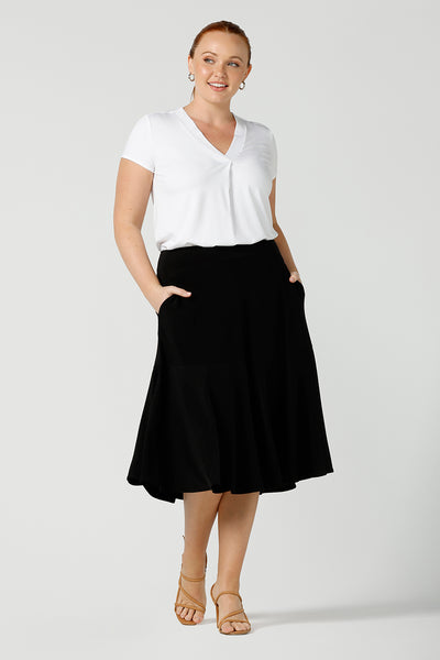 A good workwear skirt for women, this knee-length, pull-on black skirt has pockets, a ruffle hemline and comfort waistband. Worn with a V-neck, short sleeve top in white bamboo jersey, it's shown on a size 12 woman as a skirt for curvy office wear. A great addition to your capsule wardrobe, this black skirt is made by Australian made women's clothing brand, Leina & Fleur. Shop petite to plus size skirts in their online boutique in Australia. 