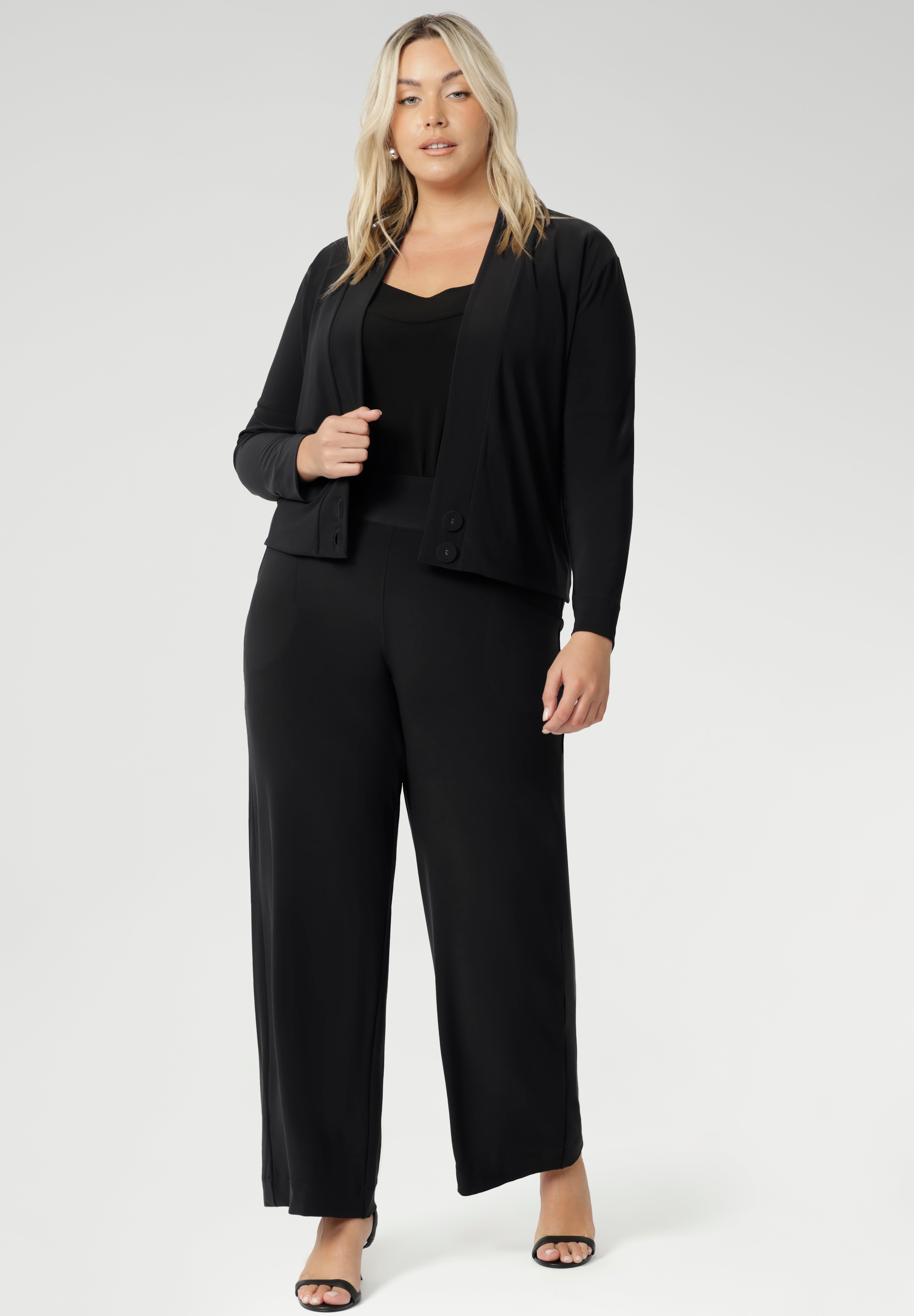 This short sleeve black jersey top is a must-have for women over 30 who appreciate timeless style and effortless versatility. Plus size woman wears her Berni Top in Black under charcoal coloured fluid suiting set, creating a comfortable yet corporate look.