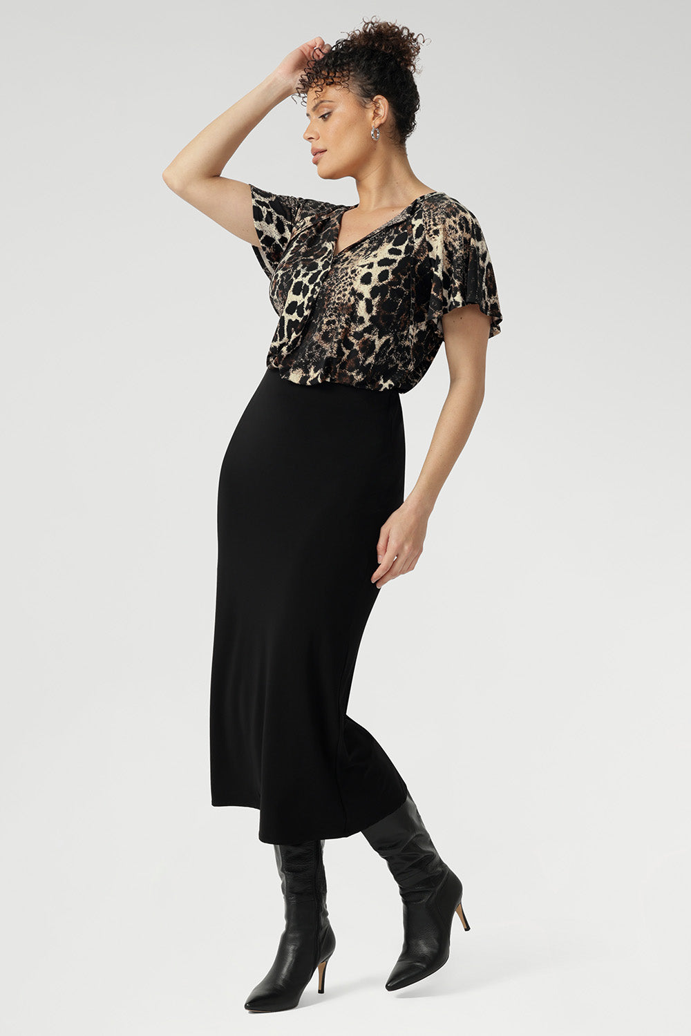 Size 10 woman wears a leopard print top with black midi skirt and black high-heeled boots creating an elegant outfit for everyday.