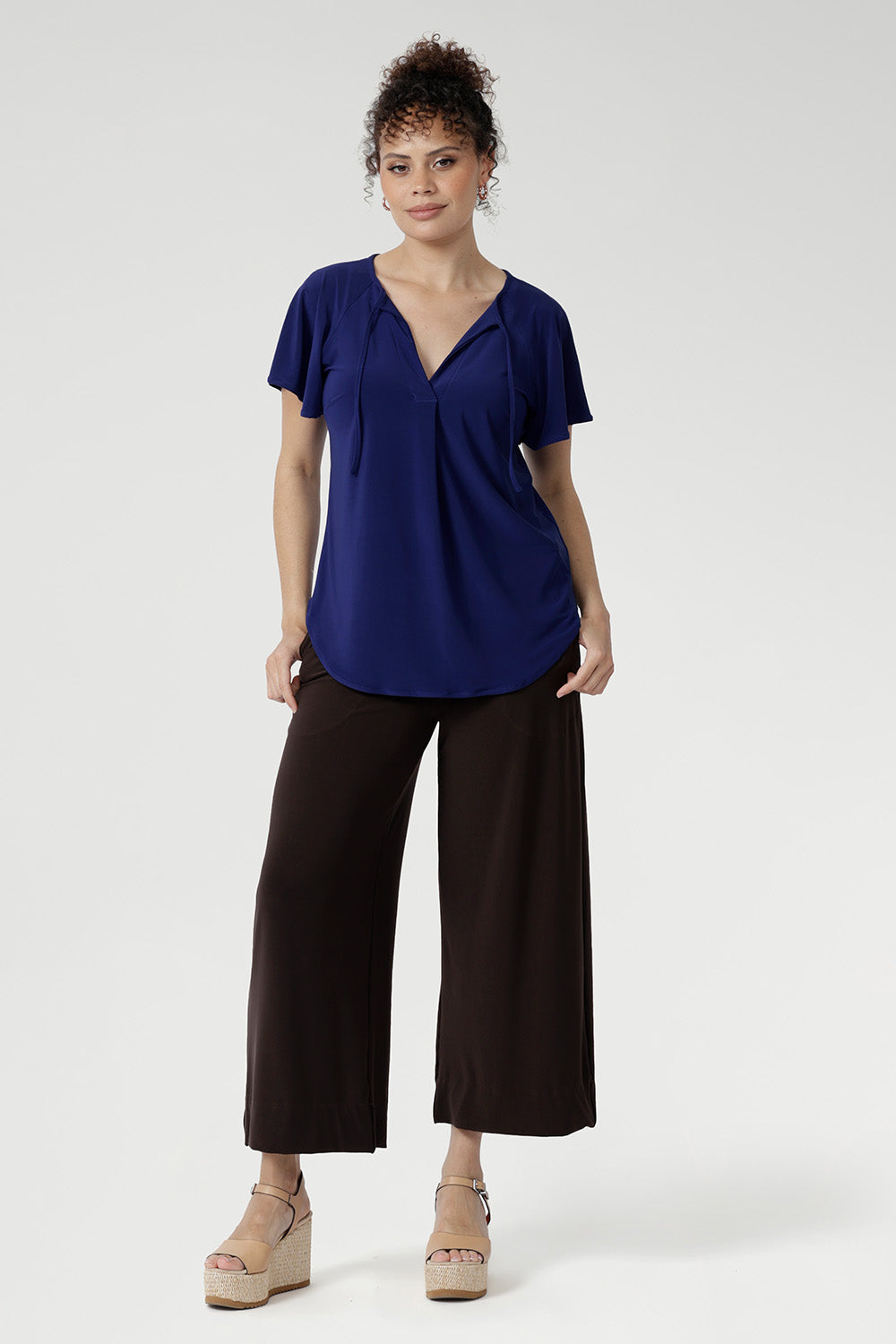 Crafted from a dry-touch jersey with gentle stretch, the Bowie Top in Sapphire offers a relaxed silhouette complemented by a V-neckline, soft pleat detailing, and tie accents. Finished with flutter sleeves and a shirttail hem, it transitions effortlessly from weekday to weekend wear.