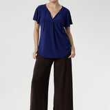 Crafted from a dry-touch jersey with gentle stretch, the Bowie Top in Sapphire offers a relaxed silhouette complemented by a V-neckline, soft pleat detailing, and tie accents. Finished with flutter sleeves and a shirttail hem, it transitions effortlessly from weekday to weekend wear.