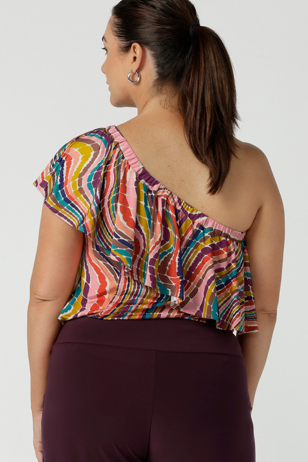 Back view of a size 12 one shoulder top woman wears an off shoulder top in vibrant rainbow swirl Briar top in soft slinky jersey. Made in Australia for women size 8 - 24.