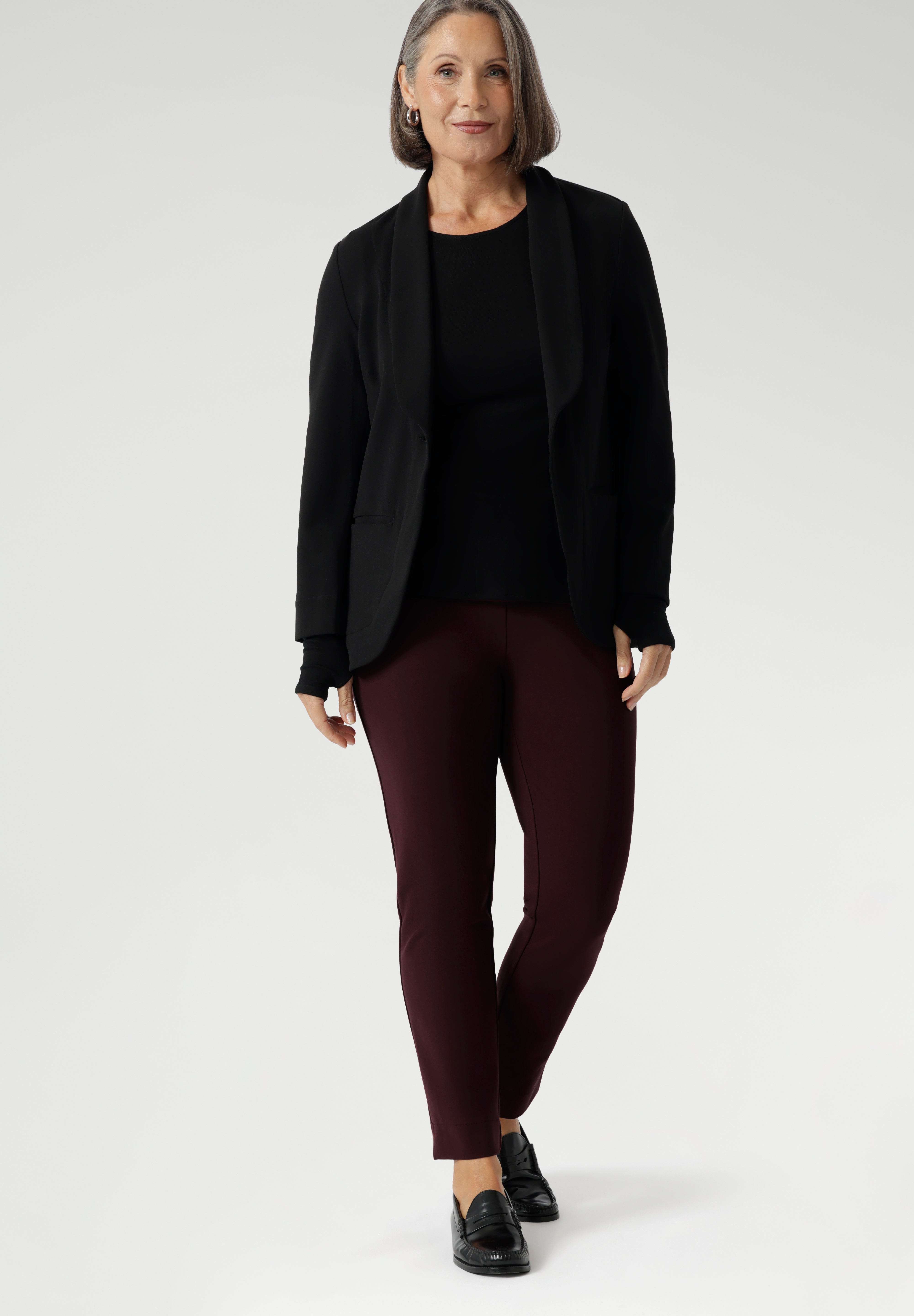 Size 10 woman wears knit top under black work wear blazer. Designed for comfort and versatility, it features a flattering close-to-body fit that moves with you, thanks to its generous stretch and breathable finish. Black knit top has thumbholes that can be used or tucked away for versatility in styling and extra warmth. Available in size 8-24.