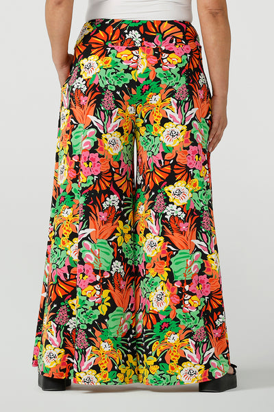 Back view of a size 12 woman wearing the Caspian Palazzo pant n a beautiful bright colourful print. In soft and lightweight jersey this pant features side pocket and a wide leg opening. Styled back with a black cami top and platform sandals. A perfect look for weekend wear. Made in Australia size 8-24.