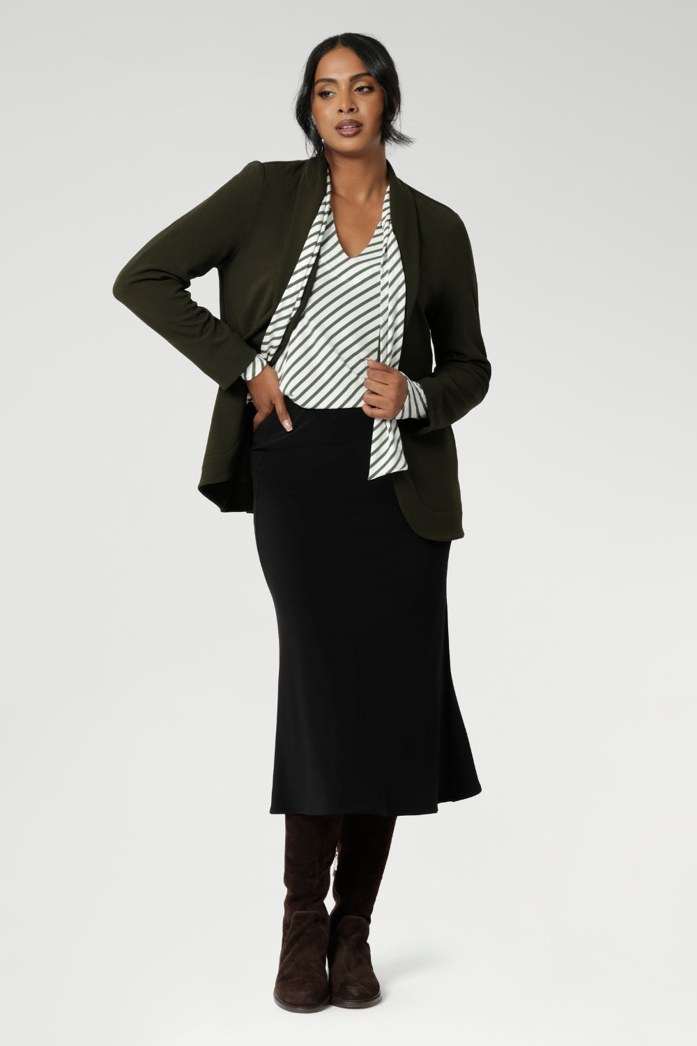 Women's black sleek midi skirt with streamlined design, can easily be dressed up for a more elevated look or worn casually - making it a truly versatile wardrobe staple for your everyday. Size 10 model pairs black midi skirt with olive striped white top, olive blazer and a long brown boots.