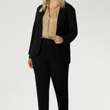 Image of plus sized woman wearing black work wear pants. The Corbin Pant is made of stretchy black Scuba Crepe fabric. This off duty pant style is breathable and has a matching black blazer to complete the full suit look. Made in Australia by Leina & Fleur, a woman's clothing brand that stocks sizes 8-24.