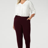 Designed with a mid-rise fit, they feature a waistband with belt loops for added styling options. The invisible front zip with an internal button ensures a sleek, clean look while providing a secure fit. Size 18 woman wears her Corbin Pants with white blouse and brown heels.