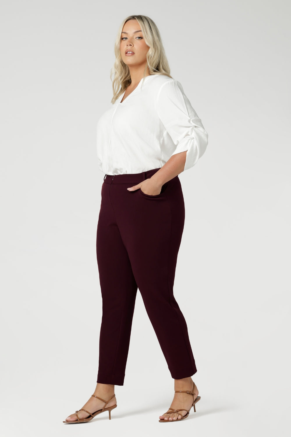 The invisible front zip with an internal button ensures a sleek, clean look while providing a secure fit. Size 18 woman wears her Corbin Pants with white blouse and brown heels.
