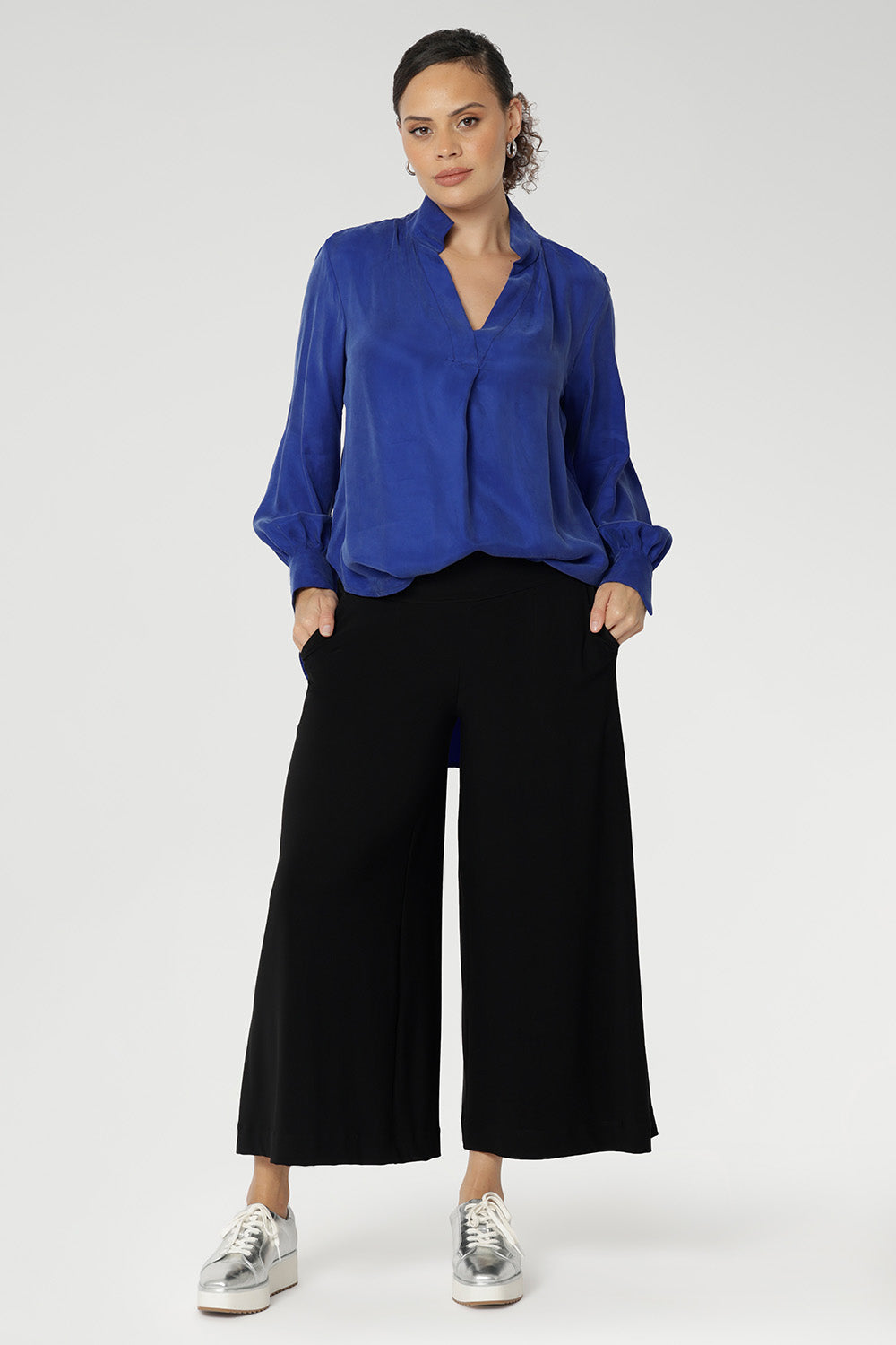 A size 10 woman wears black wide-leg pants and Bright Cobalt top. Cropped in length, the black pants have a smooth waistband, side pockets and are pull-on pants made in stretch jersey. Made in Australia, the pants are size inclusive in sizes 8 - 24.