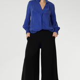A size 10 woman wears black wide-leg pants and Bright Cobalt top. Cropped in length, the black pants have a smooth waistband, side pockets and are pull-on pants made in stretch jersey. Made in Australia, the pants are size inclusive in sizes 8 - 24.