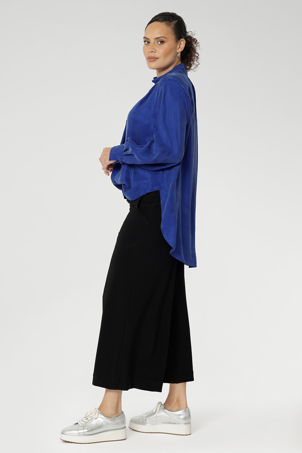 A size 10 woman wears black wide-leg pants made from easy care dry touch jersey. Cropped in length, the black pants have a smooth waistband, side pockets and are pull-on pants made in stretch jersey. Made in Australia, the pants are size inclusive in sizes 8 - 24.