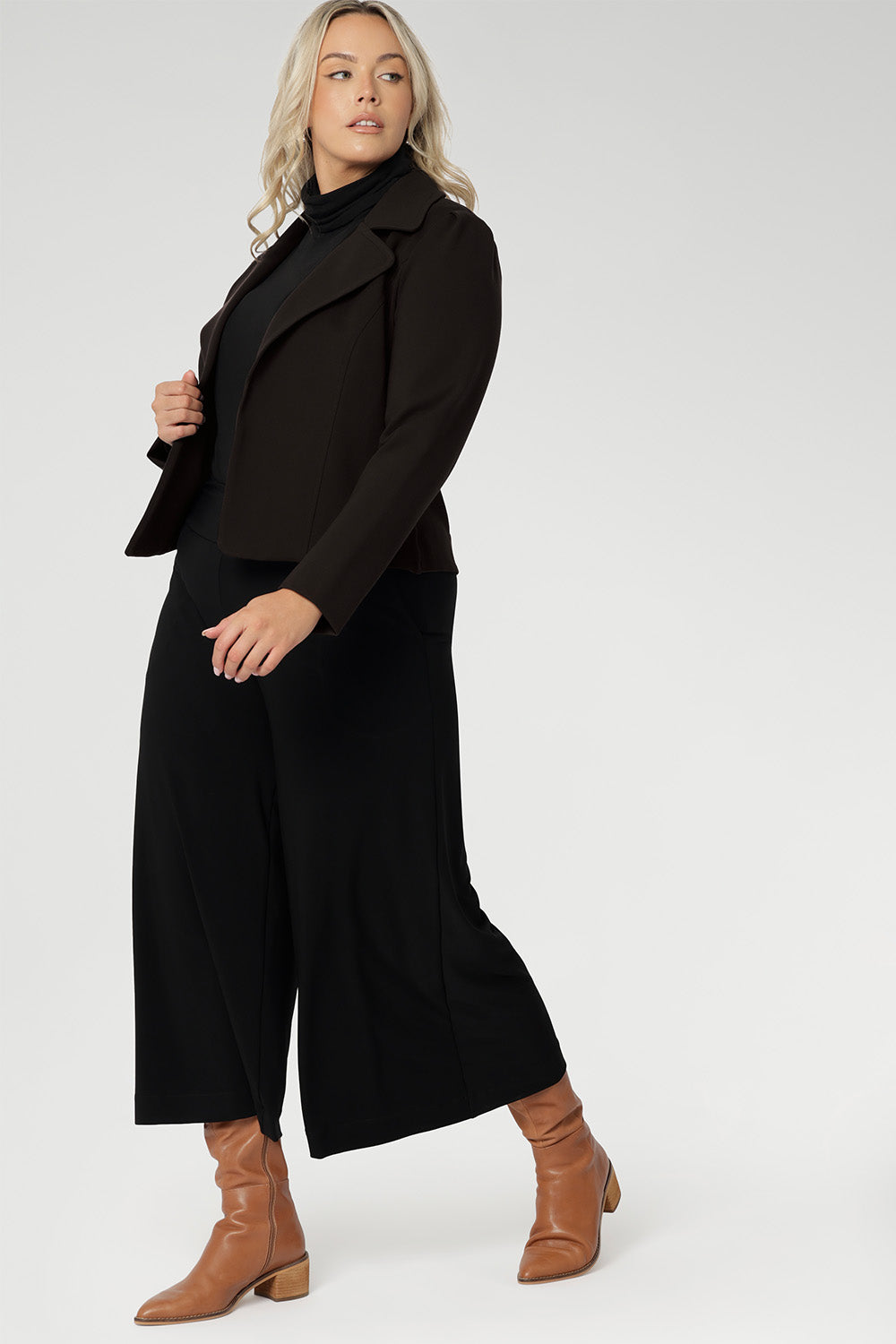 Plus size woman wears black culottes with black turtle neck & brown jacket. Stretch black pants for women, have a smooth waistband, side pockets and are a pull-on style. Made in Australia, from dry touch jersey fabric in sizes 8-24.