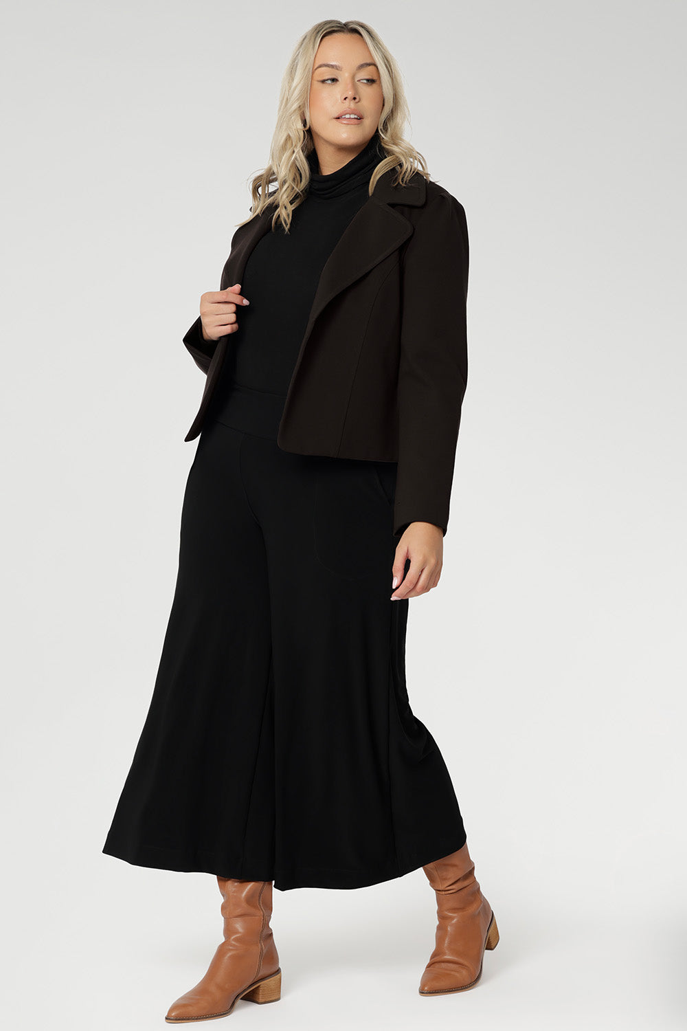 Plus size woman wears black culottes with black turtle neck & brown jacket. Stretch black pants for women, have a smooth waistband, side pockets and are a pull-on style. Made in Australia, from dry touch jersey fabric in sizes 8-24.