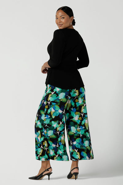 Back view of a size 10 woman wears the Dany culotte in Canopy, a full leg culotte with a canopy print. A bold green colour splatter print. Styled back with pink heels and a navy wrap top. Made in Australia for women size 8 - 24.
