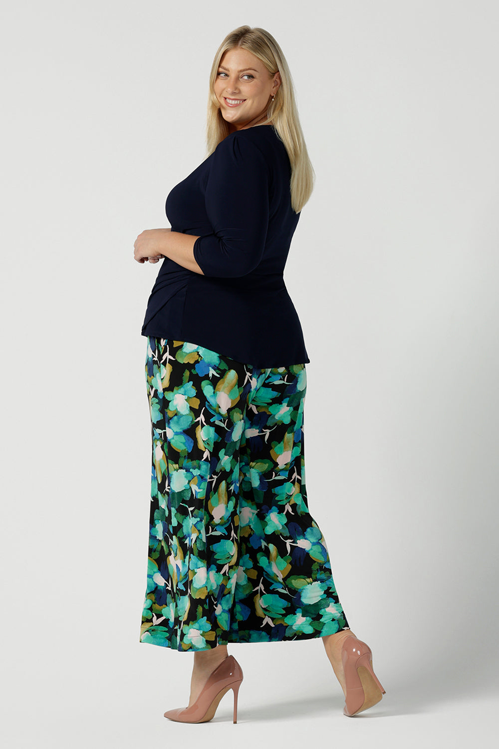 Back view of a size 18 woman wears the Dany culotte in Canopy, a full leg culotte with a canopy print. A bold green colour splatter print. Styled back with pink heels and a navy wrap top. Made in Australia for women size 8 - 24.