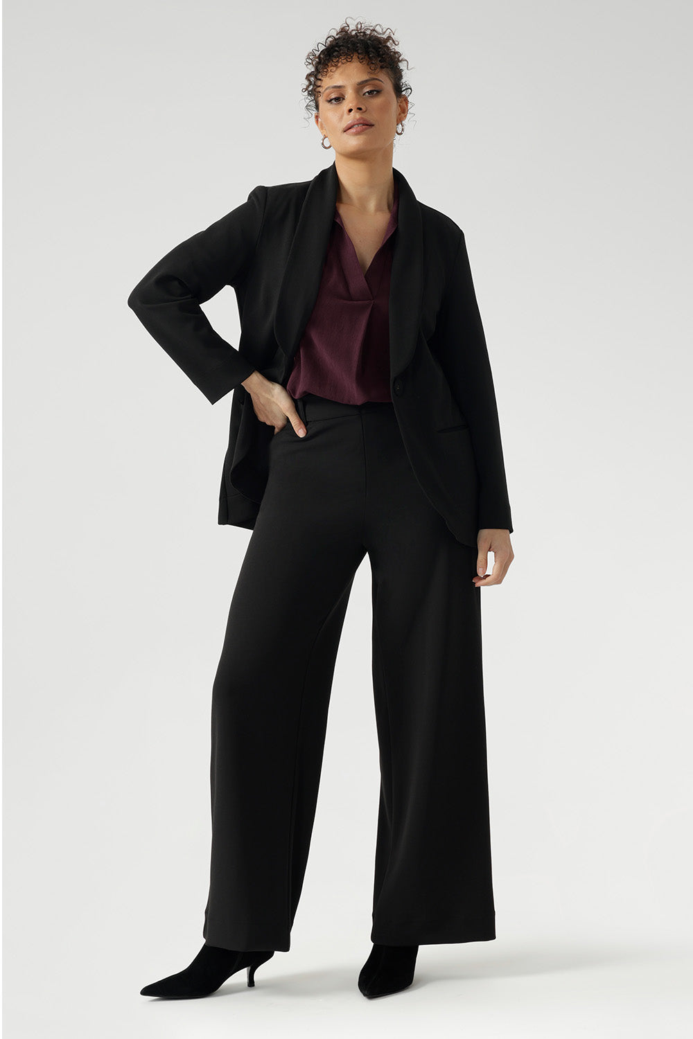 Full body back image of tall woman wearing. Black work wear pants. Easy care fabric used to craft pants is scuba crepe. Off duty pants provide breathable stretch and comfort. Australia Made for woman in Australia and New Zealand. Leina & Fleur is a woman’s clothing brand that has sizes ranging from 8 to 24 including short and regular lengths pants.
