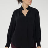 A size 10 woman wears the Ellis shirt in Graphite Black styled with wine coloured skinny leg pants, cresting a corporate casual look. Available in sizes 8-24.