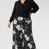 Plus size woman wears the Ellis shirt in Graphite Black styled tucked into printed wide leg pants and black heels for an elevated stylish.