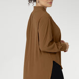 Plus size woman wears lightweight, easy to wear shirt that holds its shape without stretch. In the warm neutral shade of Nuthatch, it brings subtle sophistication to everyday dressing. The full-length sleeves are finished with clean cuffs and covered buttons — an understated touch that elevates the look. A gently curved shirttail hem sits longer at the back, offering balanced proportions and flattering coverage. Available in size 8-24.