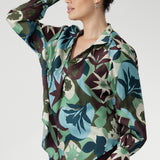The bold abstract print blends rich tones of green, blue, and plum, making it a standout for both professional and social settings. A sophisticated collared V-neckline with tailored centre tuck adds structure, while the full-length cuffed sleeves with covered buttons bring a polished finish.