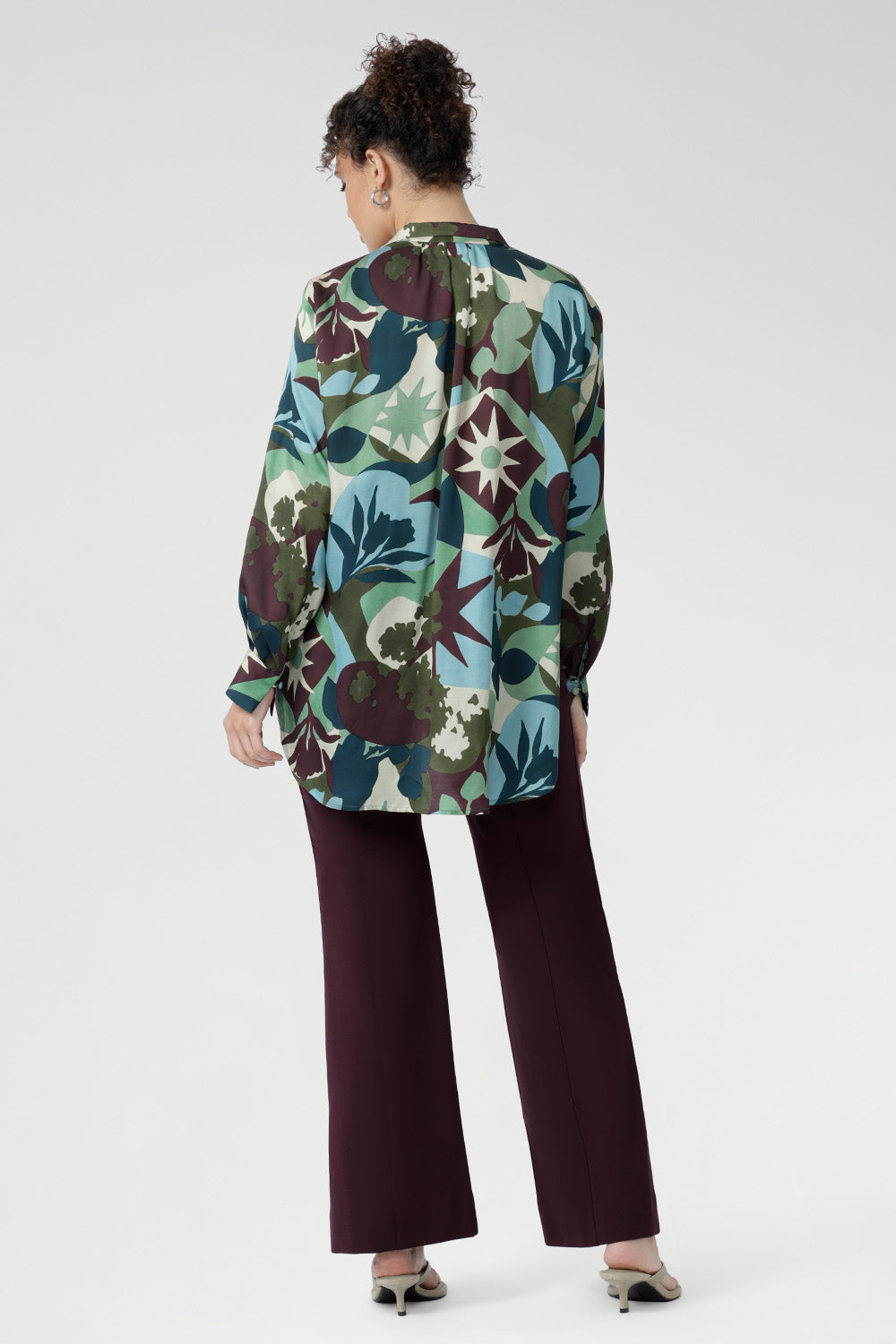 Sharp collared V-neckline and soft tailored details create a flattering shape, while full-length sleeves with covered button cuffs add a refined touch. Featuring a vibrant abstract print in rich green, blue, and plum tones, this shirt turns heads from office to evening.